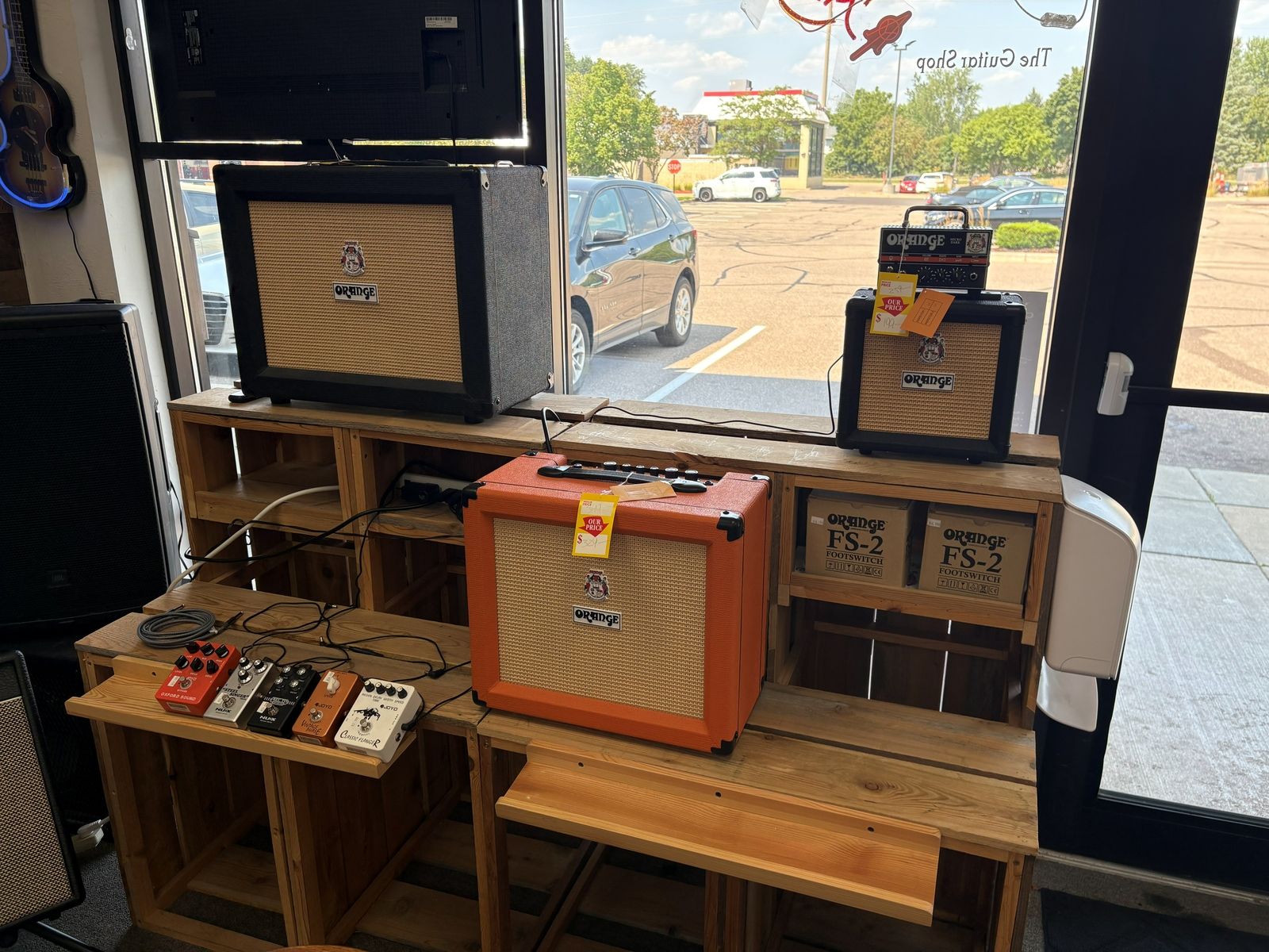 Orange practice amps and a pedal board on the reclaimed wood bench by the front window