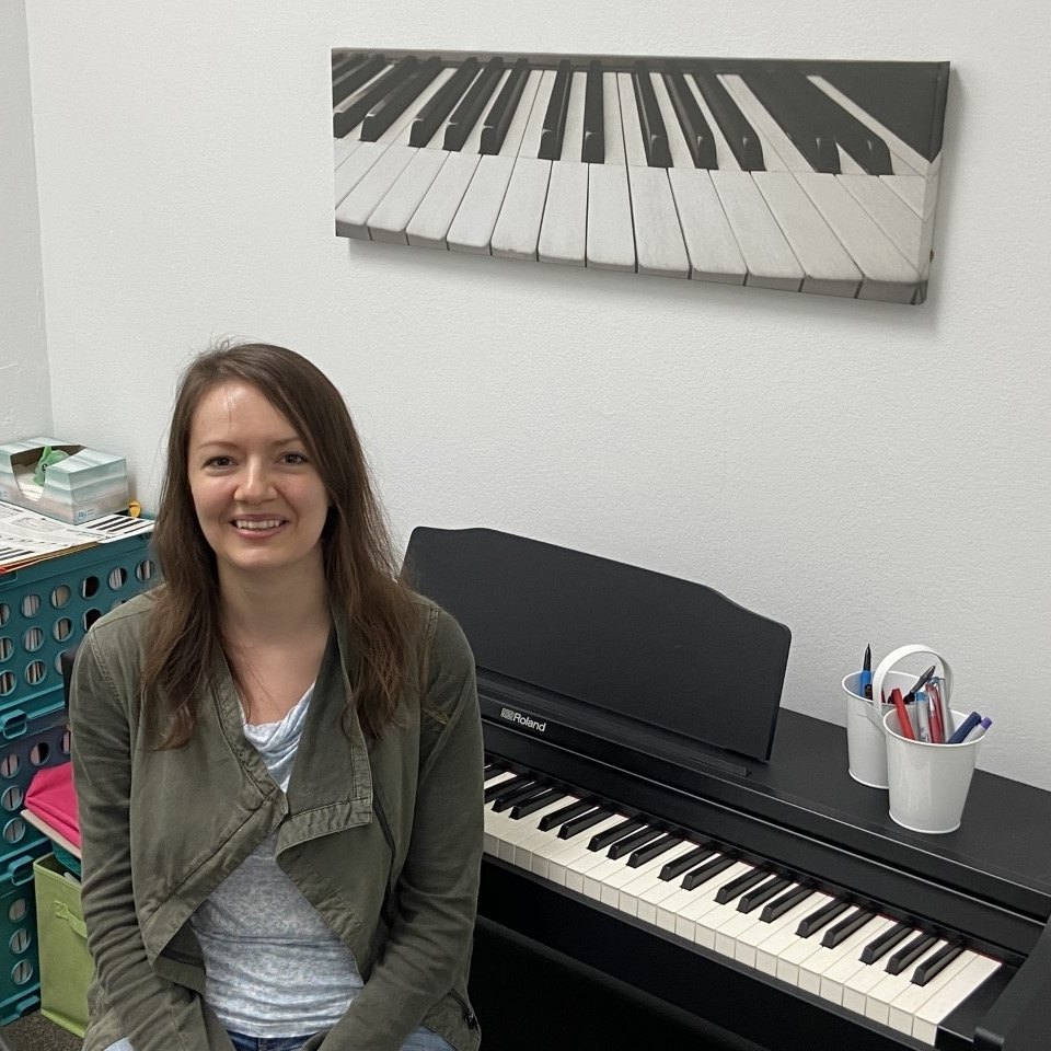 Piano teacher seated at the Roland digital piano beneath a piano-keys canvas
